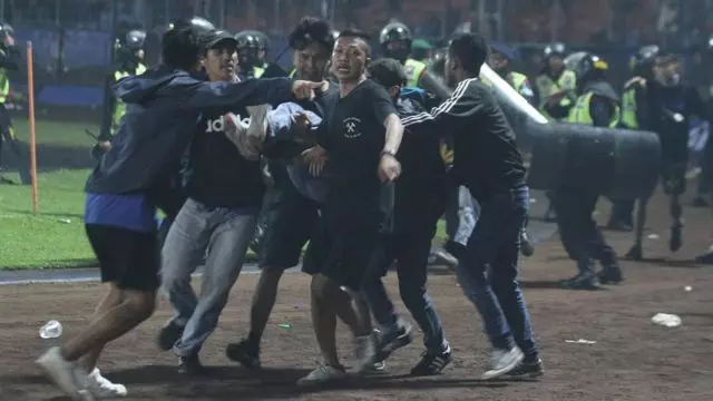 Sejumlah penonton membawa rekannya yang pingsan akibat sesak nafas terkena gas air mata yang ditembakkan aparat keamanan saat kericuhan usai pertandingan sepak bola BRI Liga 1 antara Arema melawan Persebaya di Stadion Kanjuruhan, Malang, Sabtu (1/10/2022). 