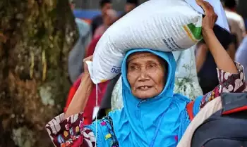 Seorang warga menjunjung bantuan pangan beras 10 kilogram (kg) dari pemerintah